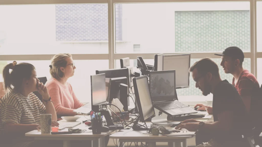Equipo trabajando en oficina frente a ordenadores, representando la dinámica de comunicación en equipos de trabajo