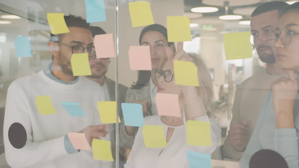Equipo colaborando con notas adhesivas en una pared de cristal durante una sesión de trabajo